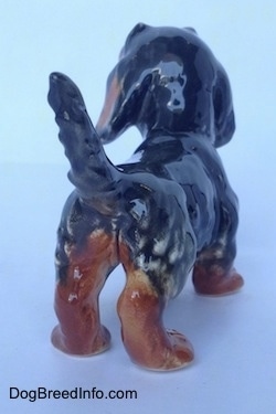 The back right side of a black and brown Dachshund figurine in a standing pose with its tail up. The figurine is glossy.