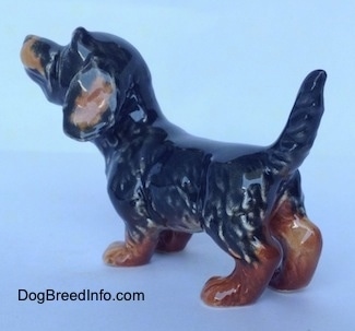 The back left side of a figurine of a black and brown Dachshund in a standing pose with its tail up. The figurine has detailed hair shapings.