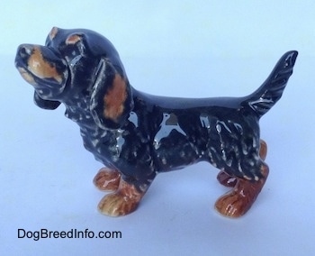 The left side of a black and brown Dachshund figurine in a standing pose. The figurine has short detailed furry legs.