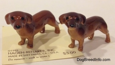 The front left side of two Dachshund Mama standing figurines. The figurines have long bodies and short legs.
