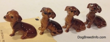 Four different Dachshund Pup Seated figurines have long tails relative to there sides.