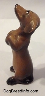 The left side of a brown with black Dachshund puppy in a begging pose figurine. The figurine has a thin tail that is hard to differentiate from its body.