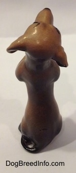 The back of a brown with black Dachshund puppy in a begging pose figurine. The ears of the figurine are out away from its head and it has a long body.