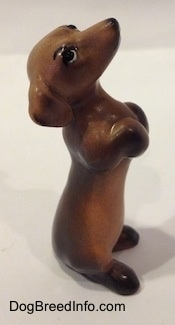 The right side of a brown with black Dachshund puppy in a begging pose. The figurine has short legs and its eyes are detailed.
