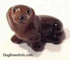The front left view of a Dachshund sitting figurine. The figurine has black circles for eyes and a nose.