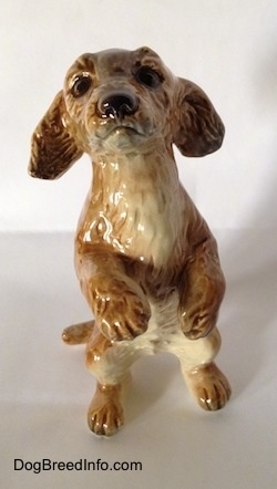 A porcelain figurine of a tan Dachshund in a begging pose. The figurine has accurate face details and its paws are in the air.