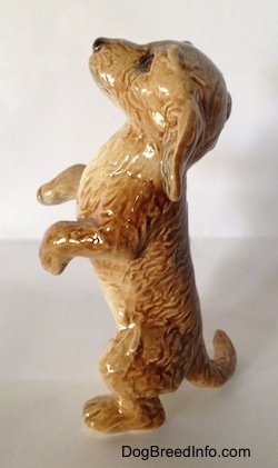 The left side of a porcelain figurine that is a tan Dachshund in a begging pose. The figurine has a long body and fine hair details.