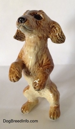 A tan porcelain Dachshund figurine that is in a begging pose. The figurine has detailed furry paws.