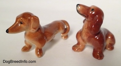 The front left side of a sitting Dachshund and a standing Dachshund figurine. The ears of the figurines are hard to differetiate from there bodies.