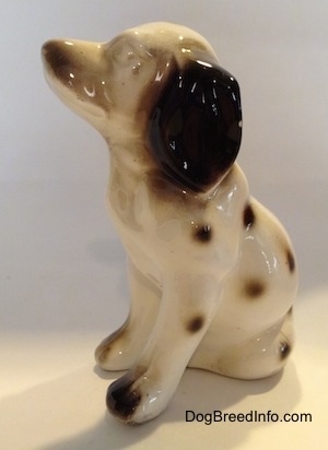 The front right side of a Dalamatian figurine in a sitting pose that has no eyes painted on it. The figurine has black tipped paws.