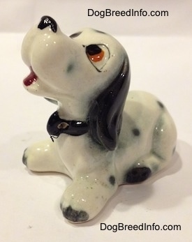 The front left side of a Dalmatian puppy figurine. The figurine has an open mouth and it is wearing a collar.