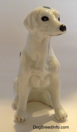 The front of a Dalmatian puppy in a sitting pose figurine. The figurine has a detailed chest and it black nails at the top of its paws.