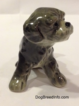 A figurine of a black and gray Dandie Dinmont Terrier puppy that is in a sitting position. It is hard to differentiate the ears of the figurine from the head.
