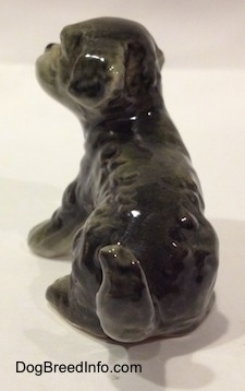 The back of a black and gray Dandie Dinmont Terrier puppy in a sitting position figurine. The figurine is glossy and it has fine hair details.