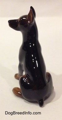 The back of a black and brown Doberman Pinscher with its paw up figurine. The figurine has a short tail and its ears are cropped.