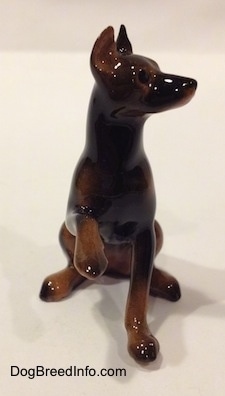 A figurine of a black and brown Doberman Pinscher with its paw up. The figurine has long legs and small paws.