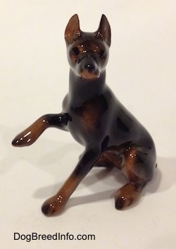 The left side of a black and brown Doberman Pinscher with its paw up figurine. The figurine has a very detailed face.