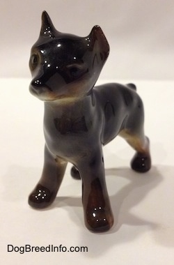 The front left side of a Doberman Pinscher puppy figurine. The figurine has short legs and small paws.