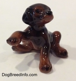 A figurine of a miniature black and brown Doberman Pinscher puppy with its paw up figurine. It is hard to tell the difference between the figurines ears and head.