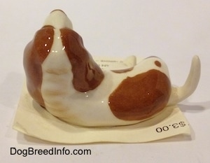 The back of a figurine of a white with brown Curbstone Setter figurine in a lying down pose. The ears of the figurine are attached to the body of the figurine.
