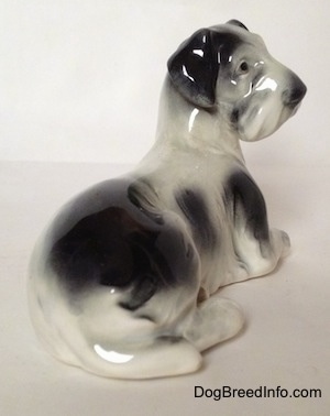 The back right side of a white and black Doxie figurine that is laying down. The figurine has a tail that is hard to differentiate from its body. It has small black eyes and a boxy looking snout.