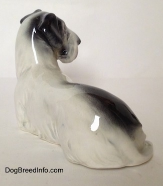 The back left side of a white and black Doxie laying down figurine. The figurine is glossy.