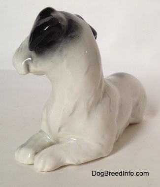 The front left side of a figurine of a white and black Doxie laying down. The figurine has black ears.