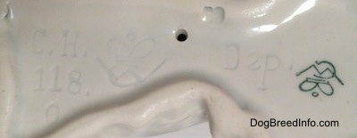 Close up - The underside of a Doxie figurine. On the underside there is a small hole, There is a Goebel Crown Mark stamped and engraved on the underside. Also engraved is the letter/number combination CH 118.0.
