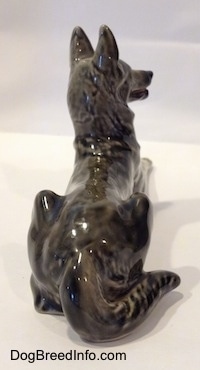 The back of a lying porcelain black with gray and white East-European Shepherd. The figurine has a long tail along its right side.