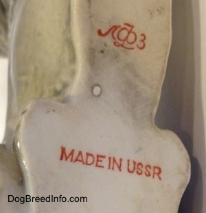 Close up - The underside of a porcelain laying East-European Shepherd figurine. Therre is the red stamp of the USSR on the underside and also the Lomonosov stamp is above it.