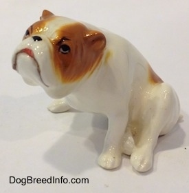 The front left side of a white with red Bulldog figurine that is in a sitting pose. The mouth of the figurine is painted like it is open.