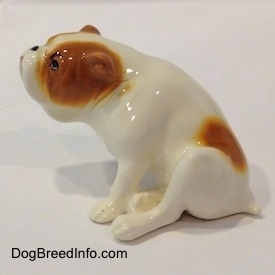 The left side of a white with red Bulldog figurine that is in a sitting pose. The figurine is glossy.