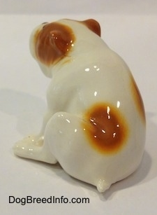 The back left side of a white with red Bulldog figurine that is in a sitting pose. The figurine has a very small tail.