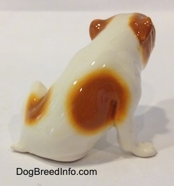 The back right side of a white with red Bulldog figurine that is in a sitting pose. It is hard to tell the difference between the ears of the figurine from the head.