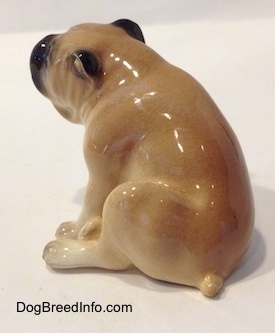The back left side of a tan and brown Bulldog figurine in a sitting pose. The figurine has black ear tips.
