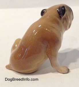 The back right side of a tan and brown Bulldog figurine in a sitting pose. The figurine is very glossy.
