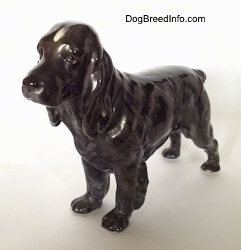 The front left side of a blue roan English Cocker Spaniel figurine. The figurine has small paws, long legs and hair on the back of the leg.