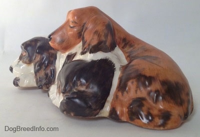 The back right side of two English Cocker Spaniels that are laying down figurine. It is hard to differentiate the tail of the figurines from the body.