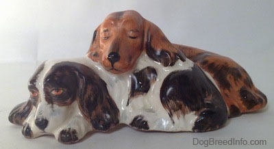 A figurine of two English Cocker Spaniel dogs that are laying down. One of the dogs is sleeping on top of the other dog which is laying down.