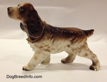 The left side of a brown and white porcelain English Cocker Spaniel figurine. The figurine has a big and long ears.