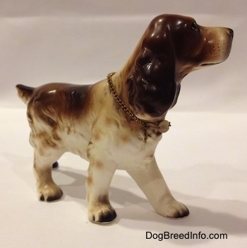 The front right side of a porcelain figurine that is of a brown and white English Cocker Spaniel. The figurine has small black tipped paws.