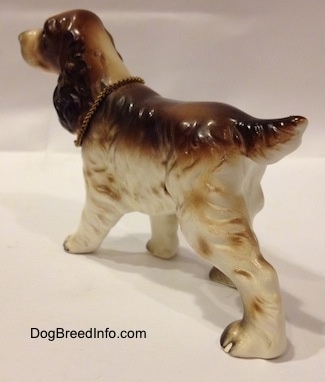 The back left side of a brown and white English Cocker Spaniel porcelain figurine. The figurine has long legs.