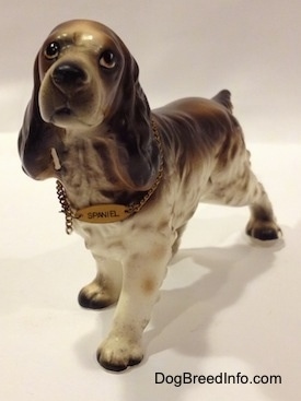 A porcelain brown and white English Cocker Spaniel figurine. The figurine is wearing a collar and on the collar there is a tag that reads - Spaniel.