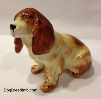 The left side of a red and white ceramic English Cocker Spaniel figurine that is in a sitting position. The side of the figurine has brown brushings to make it look like it has hair.