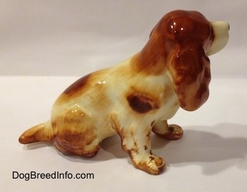 The right side of a ceramic figurine of a red and white English Cocker Spaniel in a sitting position. The figurine has a short tail.