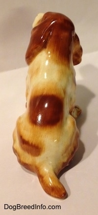 The back of a red and white English Cocker Spaniel ceramic figurine in a sitting pose. Its hard to differentiate the ears of the figurine from its body.