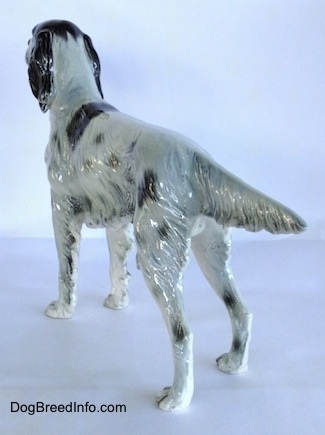 The back left side of a figurine of a black and white English Setter in a standing pose. The figurine has an extended out tail.