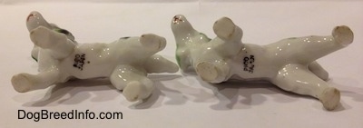 The underside of two white with green and black bone china English Setter figurines. The figurines have stamps on there undersides.