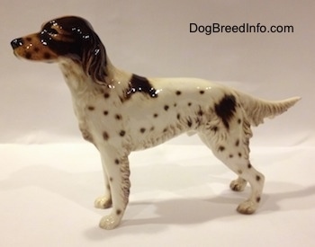 The left side of a brown and white English Setter porcelain figurine. The figurine has hair details along the trim of its body.