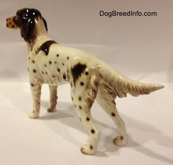 The back left side of a porcelain brown and white English Setter figurine. The figurine has brown spots on its body.